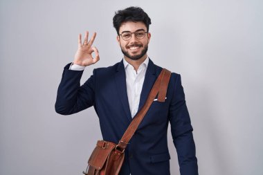 Sakallı, iş elbiseleri giymiş, gülümseyen İspanyol adam el ve parmaklarıyla imza atıyor. başarılı ifade. 