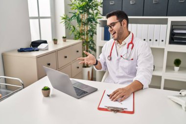 Sakallı genç İspanyol doktor klinikte online randevu veriyor başarıyı mutlu bir gülümsemeyle kutluyor ve kazanan el kaldırarak ifade ediyor. 