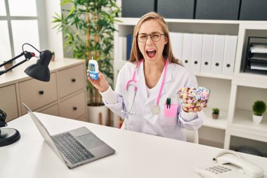 Sarışın doktor kadın elinde glukometre ve tatlı tutarak başarıyı kutluyor ve gözleri açık heyecanla bağırıyor.. 