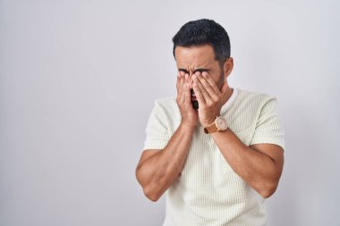 Soyutlanmış arka planda duran İspanyol sakallı bir adam yorgunluk ve baş ağrısı için gözlerini ovuşturuyor, uykulu ve yorgun bir ifade. görme sorunu 