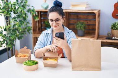 Kafkasyalı genç bir kadın evde akıllı telefon kullanarak yemek yiyor.