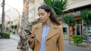 Genç ve güzel bir İspanyol kadın sokakta ciddi yüzlü akıllı telefon kullanıyor.