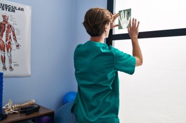 Young caucasian man physiotherapist looking xray on window at rehab clinic