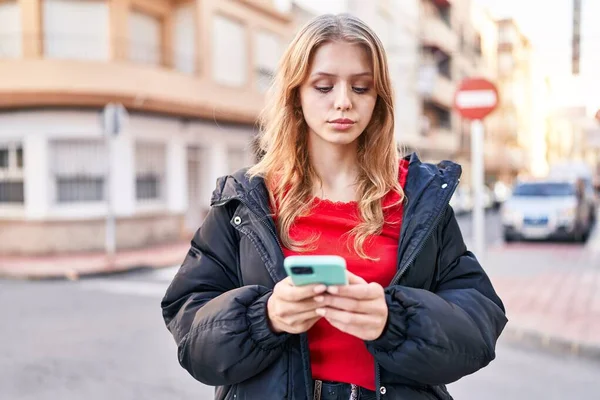 Sokakta akıllı telefon kullanan genç sarışın kadın.