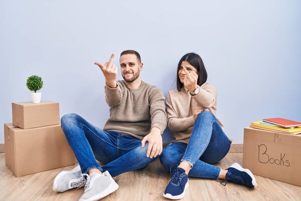 Young couple moving to a new home showing middle finger, impolite and rude fuck off expression 