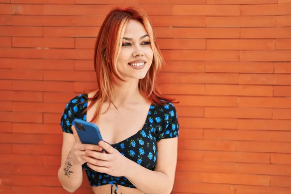 Junge Kaukasierin Lächelt Selbstbewusst Mit Smartphone Vor Isoliertem Backsteinhintergrund — Stockfoto
