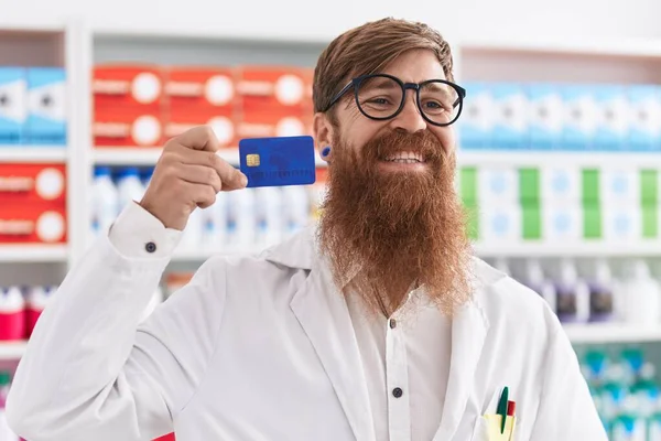 Joven Pelirroja Hombre Farmacéutico Sonriendo Confiado Celebración Tarjeta Crédito Farmacia — Foto de Stock
