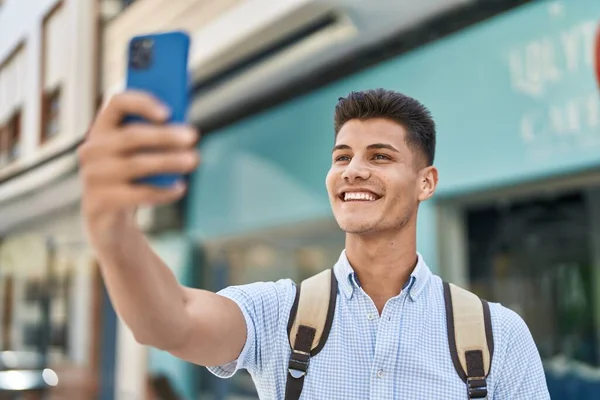 Young hispanic man student making selfie by the smartphone at street