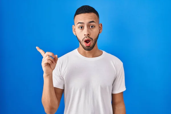 Young Hispanic Man Standing Blue Background Surprised Pointing Finger Side — Fotografia de Stock