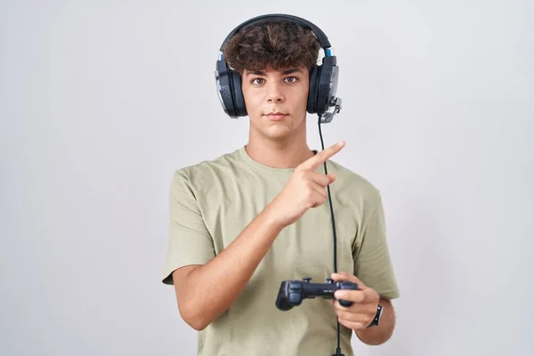 西班牙裔青少年玩电子游戏时 手持控制器 手指头指向侧面展示广告 严肃而沉着 — 图库照片