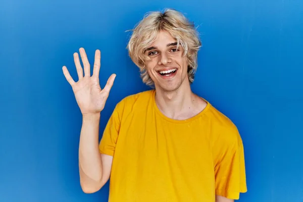 年轻的现代人站在蓝色的背景上 带着自信和快乐的微笑 用五号手指指指着 — 图库照片