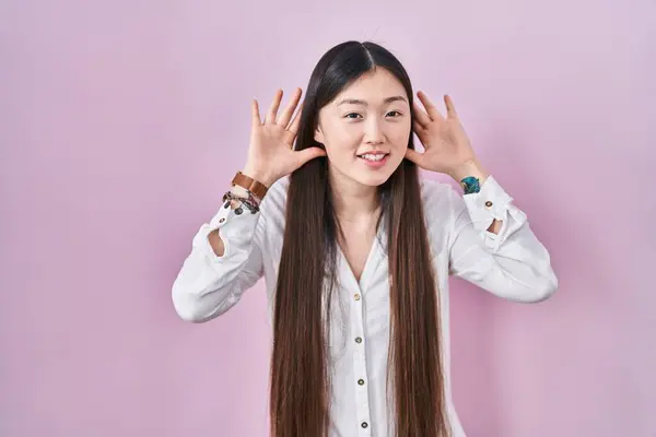 Jovem Chinesa Sobre Fundo Rosa Tentando Ouvir Ambas Mãos Gesto — Fotografia de Stock