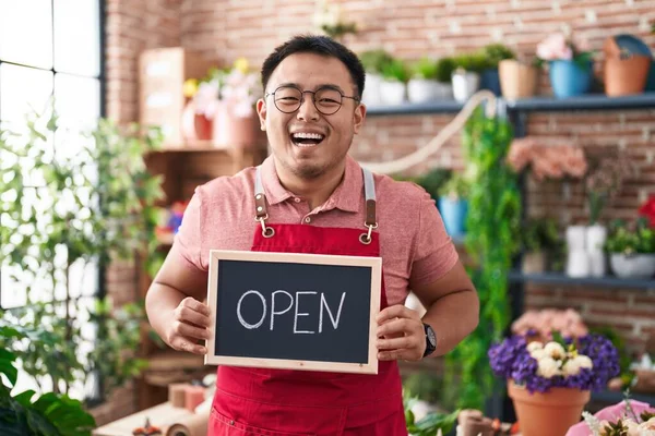 stock image Chinese young man working at florist holding open sign smiling and laughing hard out loud because funny crazy joke. 