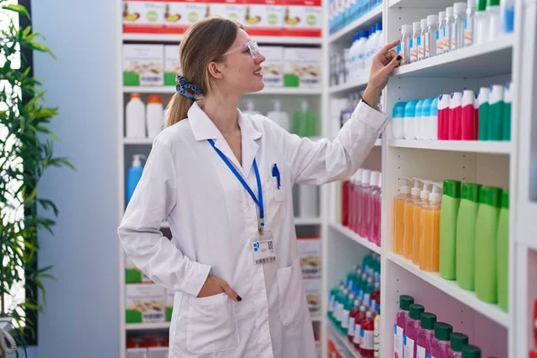 Joven Mujer Rubia Farmacéutica Sonriendo Confiado Sosteniendo Producto Estanterías Farmacia — Foto de Stock