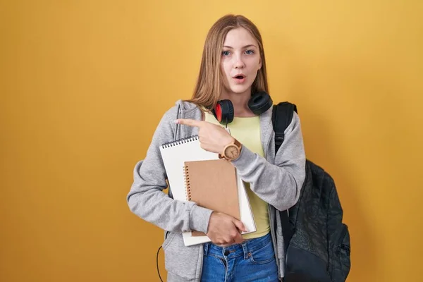 Młoda Kaukaska Kobieta Nosząca Studencki Plecak Trzymająca Książki Zaskoczona Wskazując — Zdjęcie stockowe