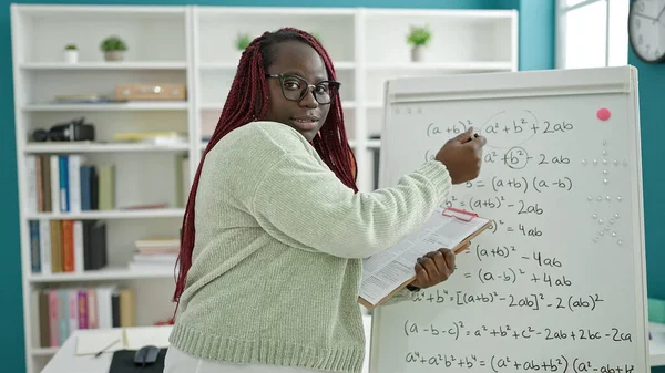 Örgü örmüş saç öğretmeni olan Afrikalı kadın üniversite kütüphanesinde matematik dersi veriyor.