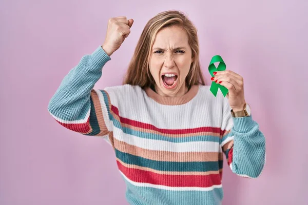 Joven Mujer Rubia Sosteniendo Apoyo Cinta Verde Molesto Frustrado Gritando — Foto de Stock