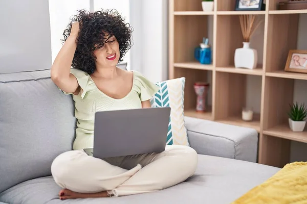 年轻的黑发女人 坐在沙发上 坐在笔记本电脑上 对问题感到困惑和好奇 拿不定主意 手拿着头思考 沉思的概念 — 图库照片