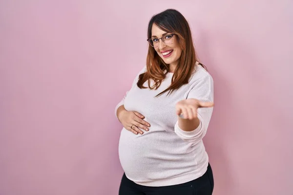 Těhotná Žena Stojící Nad Růžovým Pozadím Úsměvem Veselá Nabídka Dlaně — Stock fotografie