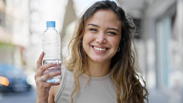 年轻美丽的惊慌失措的女人举着一瓶水在街上微笑 — 图库照片