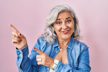 Pembe arka planda gri saçlı orta yaşlı bir kadın gülümsüyor ve kameraya bakıyor.. 