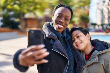 Afro-Amerikan anne ve oğlu gülümsüyor. Parktaki akıllı telefondan özçekim yapıyorlar.