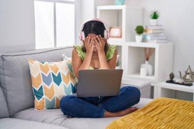 İspanyol genç kadın evde dizüstü bilgisayar kullanıyor. Ağlarken yüzünü ellerle kapatıyor. depresyon kavramı. 