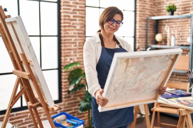 Middle age woman artist smiling confident looking draw at art studio