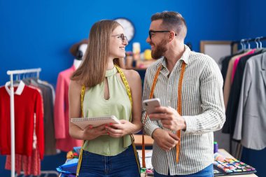 Man and woman tailors using smartphone holding notebook at clothing factory