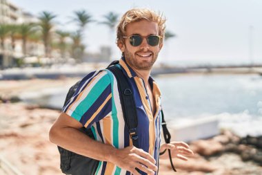 Young man tourist smiling confident wearing backpack at seaside