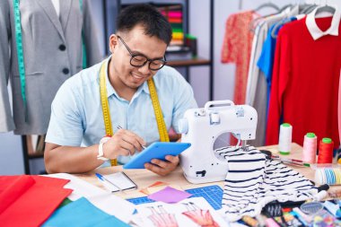 Genç Çinli terzi terzide dokunmatik ped kullanarak gülümsüyor.