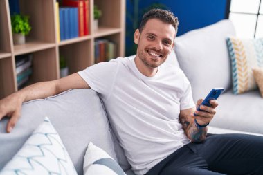Evdeki kanepede oturan, akıllı telefon kullanan genç bir İspanyol.