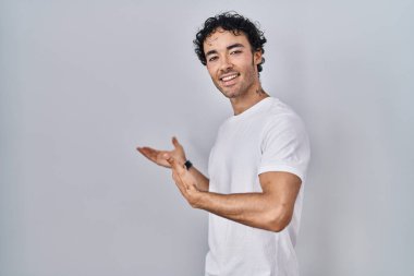 İspanyol bir adam izole edilmiş arka planda duruyor ve gülümseyerek içeri girmeye davet ediyor. 