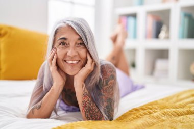 Middle age grey-haired woman smiling confident lying on bed at bedroom