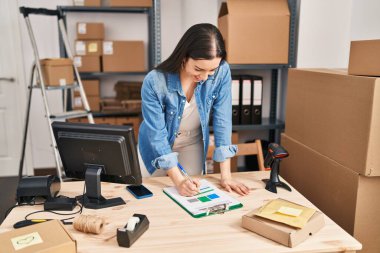Young beautiful hispanic woman ecommerce business worker writing on document at office