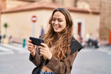 Genç ve güzel İspanyol kadın gülümsüyor. Sokakta akıllı telefondan videolar izliyor.