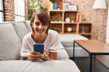 Evdeki kanepede uzanmış akıllı telefon kullanan genç, güzel İspanyol kadın.