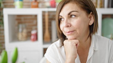 Orta yaşlı İspanyol kadın yemek odasında kendinden emin bir şekilde yan tarafa bakıyor.