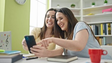 İki kadın kütüphane üniversitesinde akıllı telefon kullanarak ders çalışıyor.