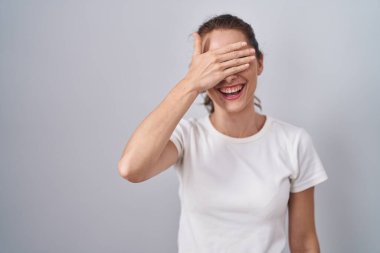 Güzel esmer kadın izole edilmiş arka planda duruyor. Gülümsüyor ve elleri yüzünde, şaşırtmak için gözleri örtüyor. kör kavram. 