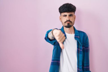 Pembe arka planda sakallı, mutsuz ve kızgın görünen, reddedilmiş ve olumsuz davranışlı genç bir İspanyol. kötü ifade. 