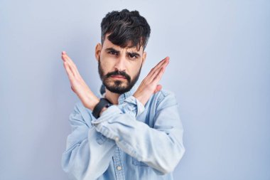 Mavi arka planda sakallı, genç İspanyol bir adam. Reddedilmiş yüz ifadesi. Kollarını kavuşturup negatif işaret veriyor. 