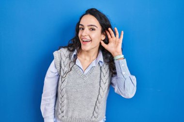 Mavi arka planda dikilen esmer bir kadın kulağından kulaklarına gülümseyerek dedikodulara ve dedikodulara kulak veriyor. Sağırlık kavramı. 