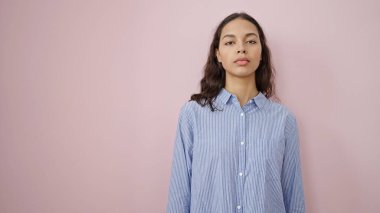 Young beautiful hispanic woman standing with serious expression over isolated pink background