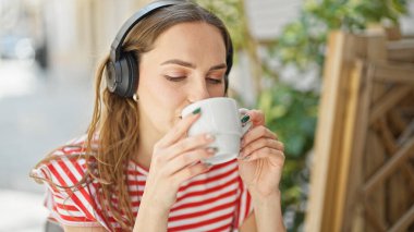 Genç sarışın kadın müzik dinliyor. Kahve dükkanının terasında kahve içiyor.