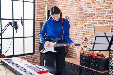 Müzik stüdyosunda gitar çalarken kendinden emin gülümseyen Çinli kadın sanatçı.