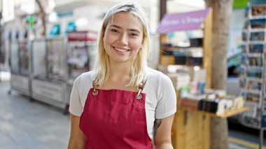 Genç, güzel, İspanyol bir kadın gazete dükkanında kendine güvenen bir önlük giyiyor.