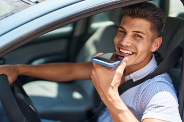 Young hispanic man talking on the smartphone sitting on car at street