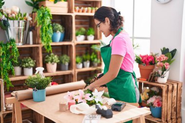 Young hispanic woman florist make bouquet of flowers at florist