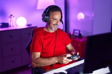 Middle age man streamer playing video game using joystick at gaming room